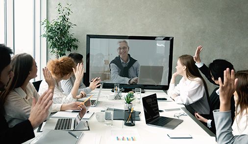 Professionals in a large conference room, video-conferencing on a large computer monitor